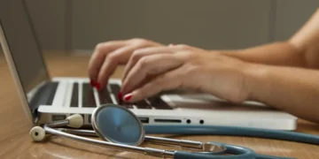 A person typing on a laptop with a stethoscope, illustrating AI connectivity software in healthcare